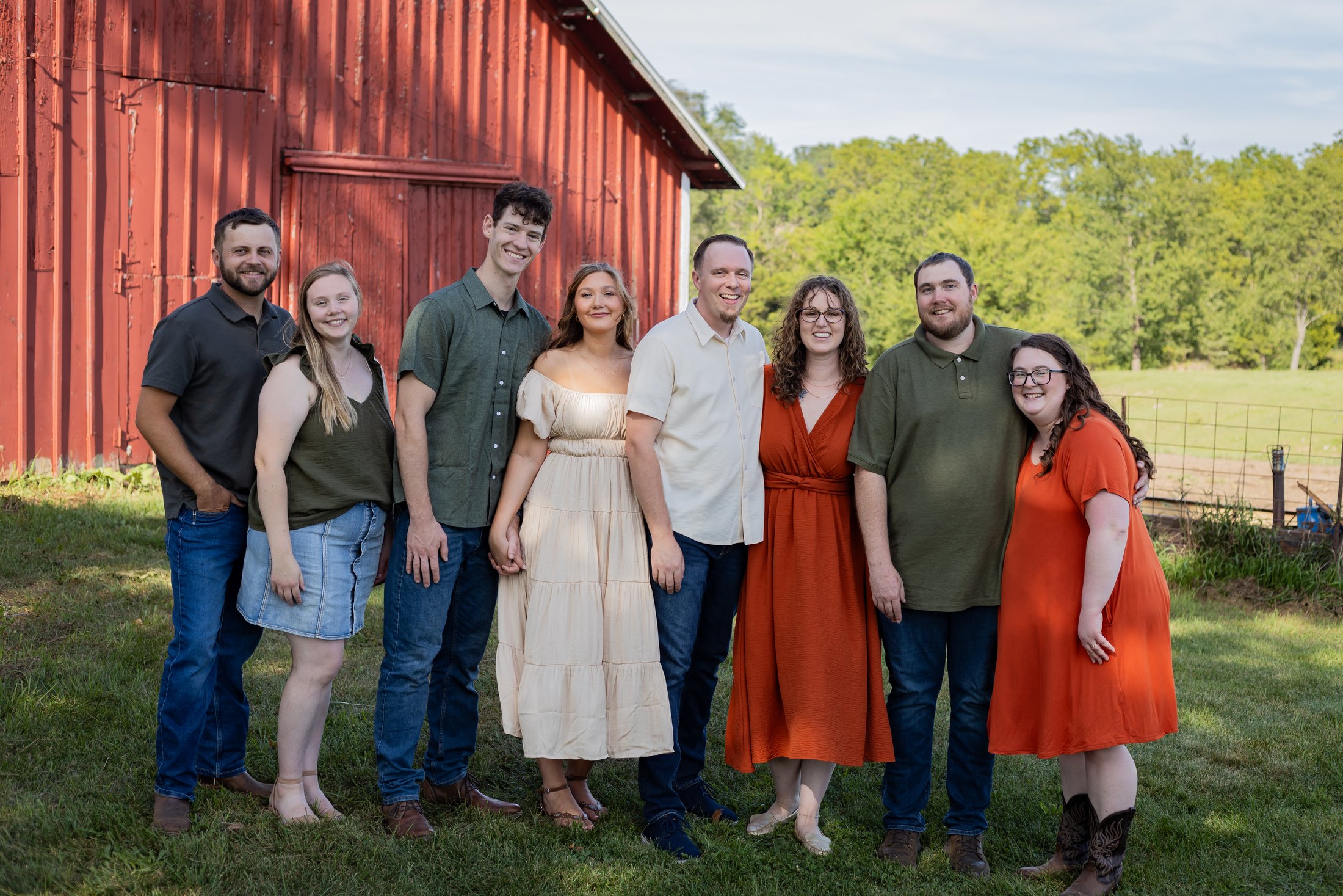 An extended family of eight gathered in warm late-day light in front of a red barn