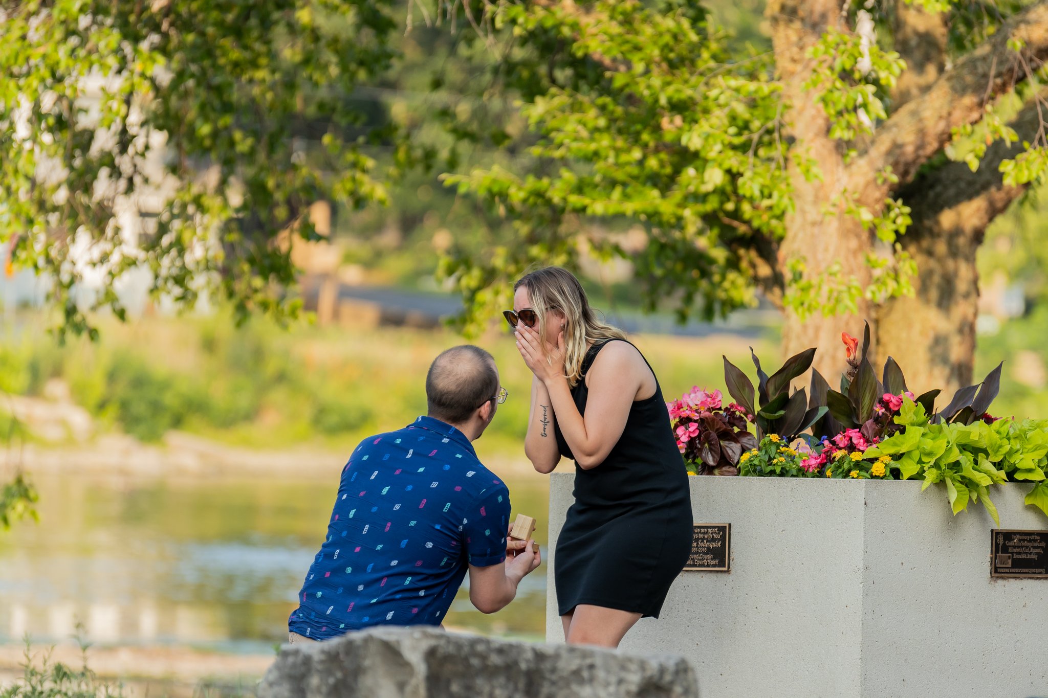 A man kneeling to propose to his partner beside a river