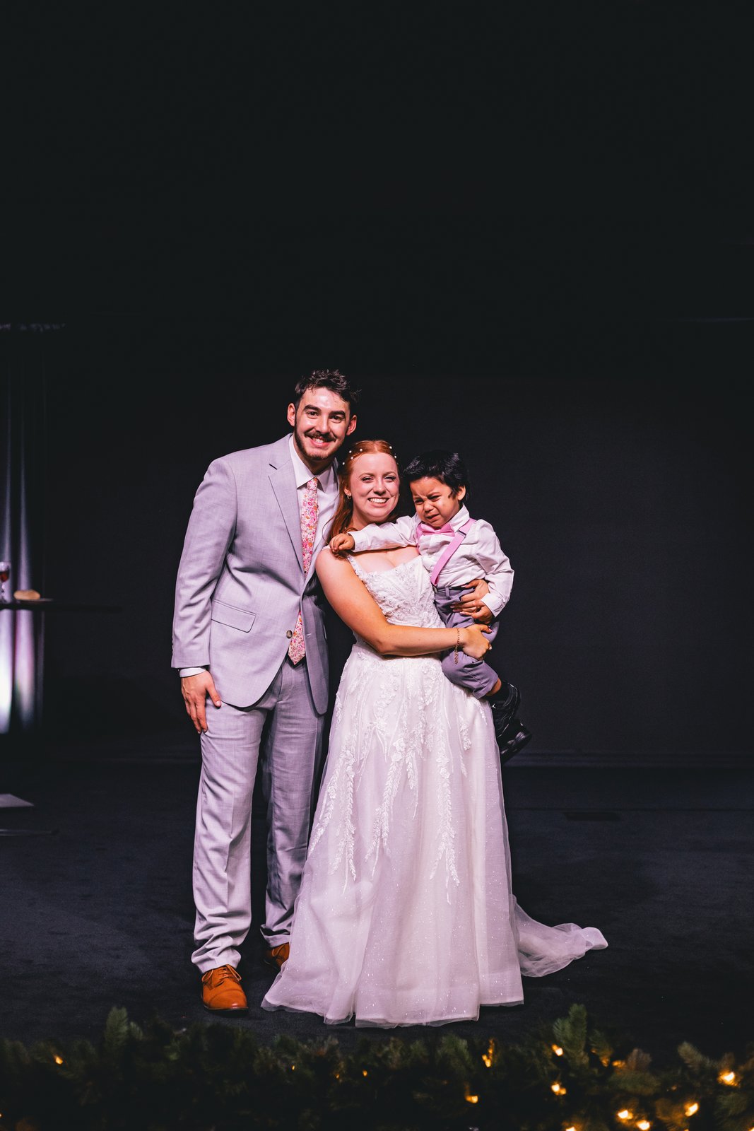 A bride and groom holding a young child on their wedding day