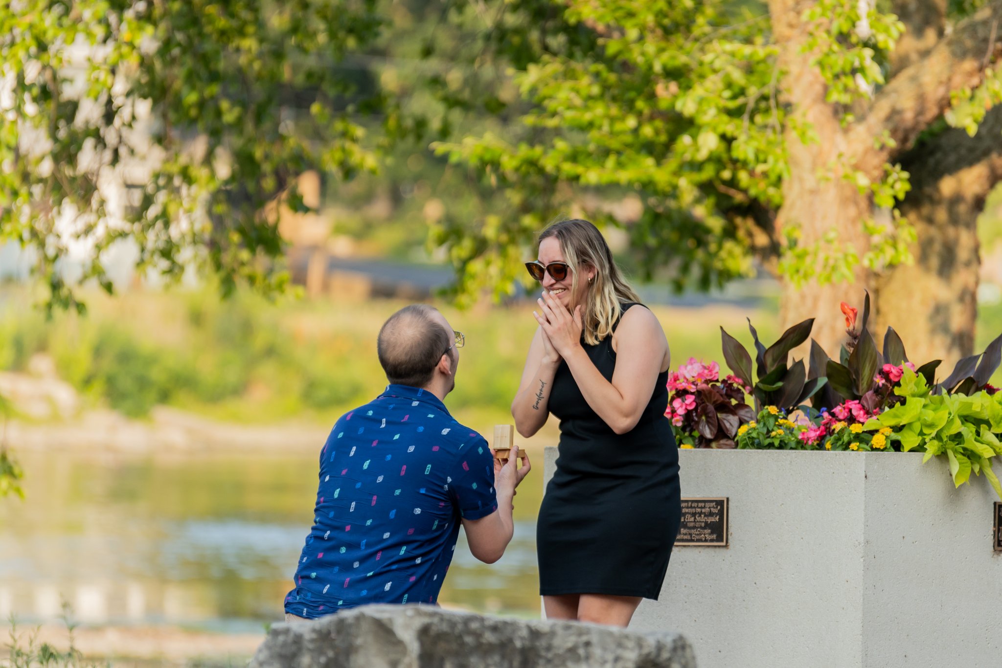 A man kneeling and holding out a ring box as his partner smiles during a proposal