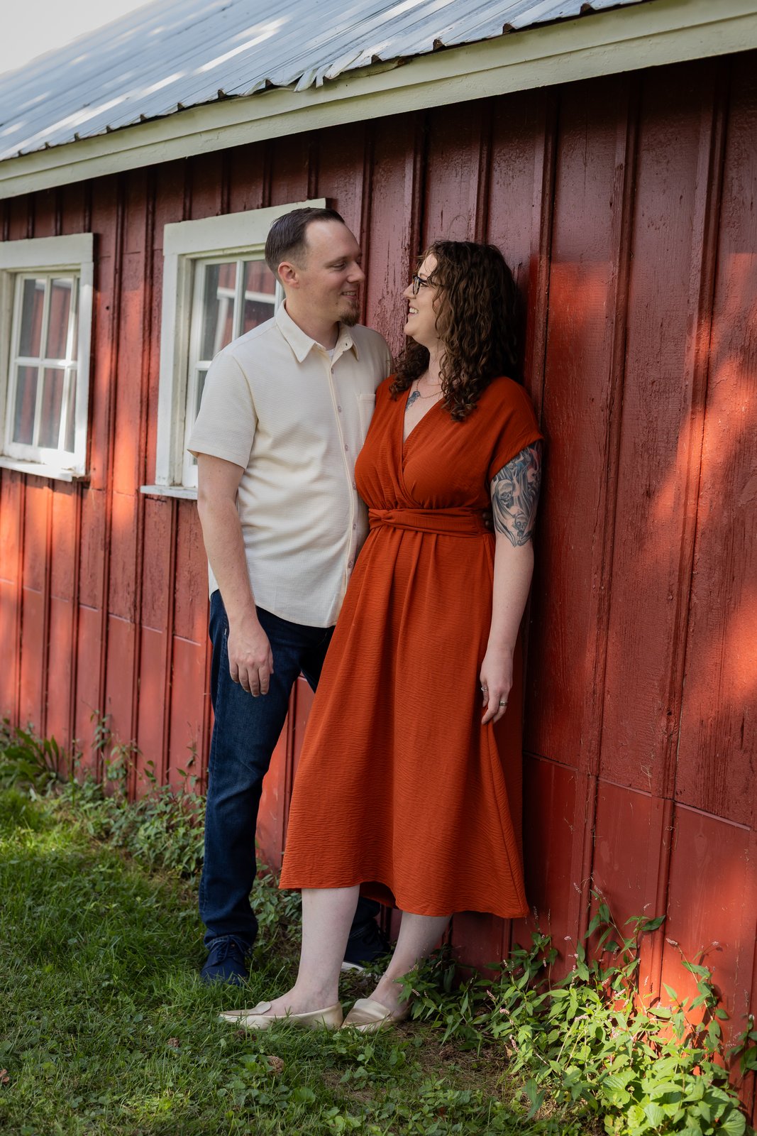 A couple standing together against a red barn wall
