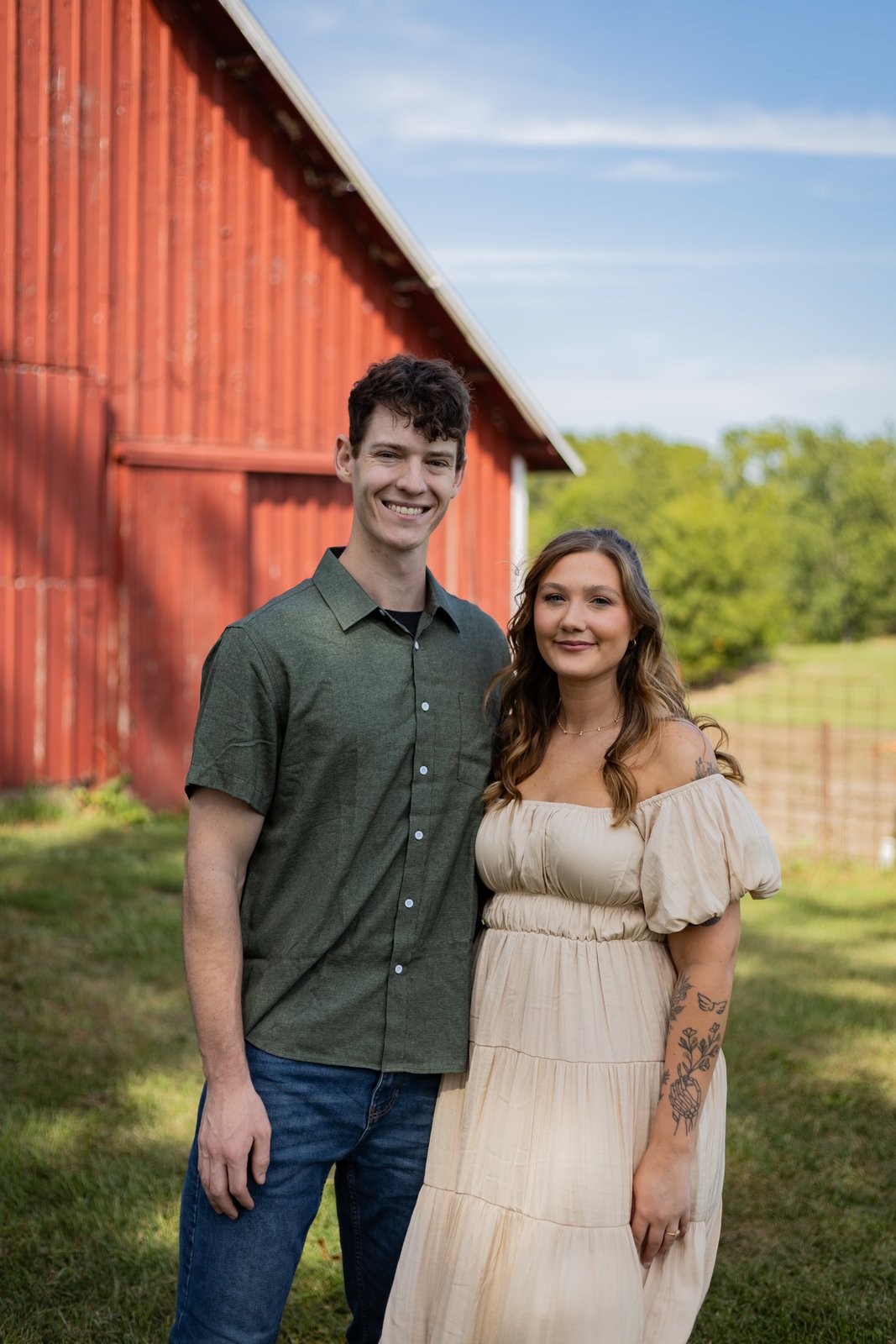 A couple posing together in front of a red barn