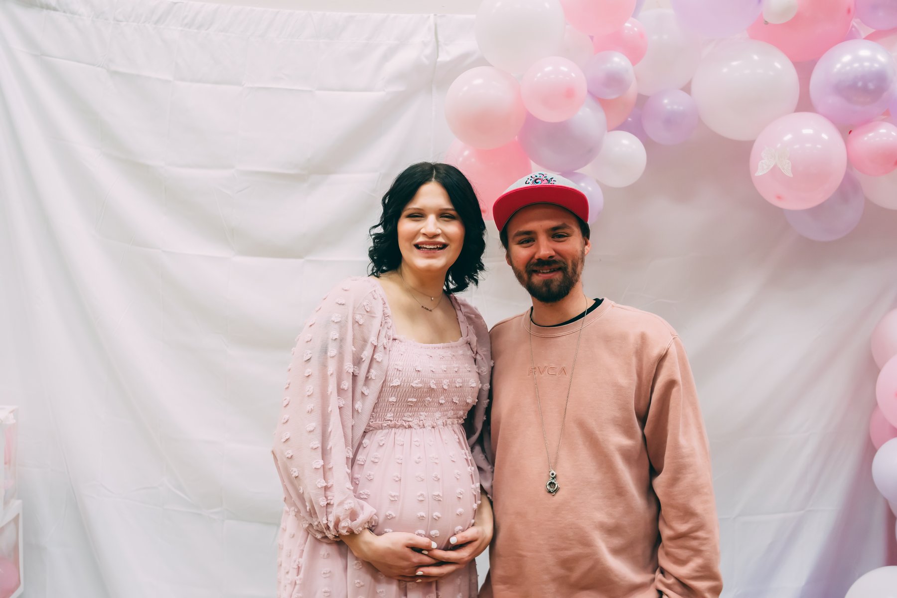 A couple at a pink and white balloon arch, the woman in a pink dress