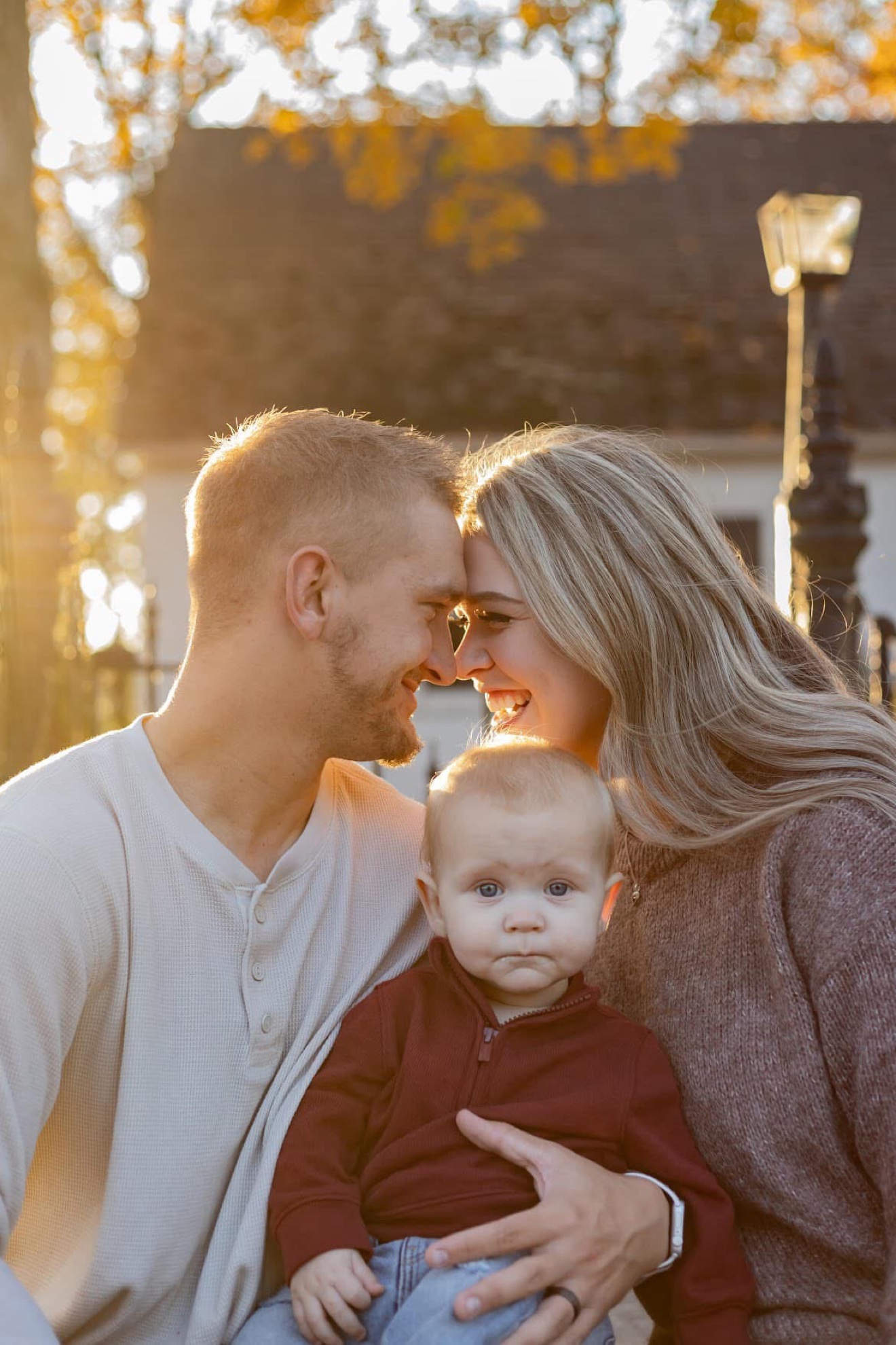 Parents smiling forehead to forehead with their baby between them in golden light