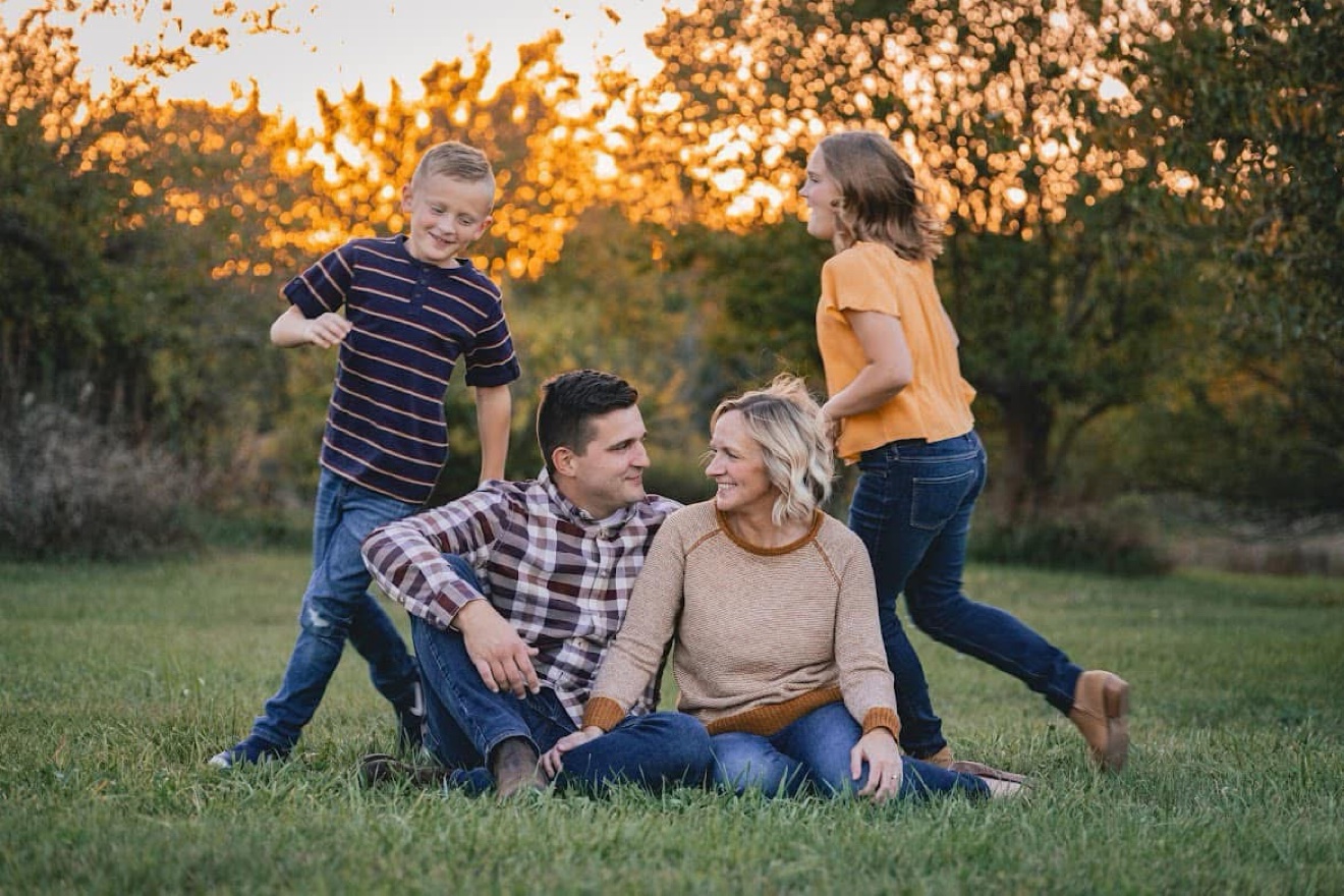 A family playing together on the grass at golden hour, parents seated while their kids run around them