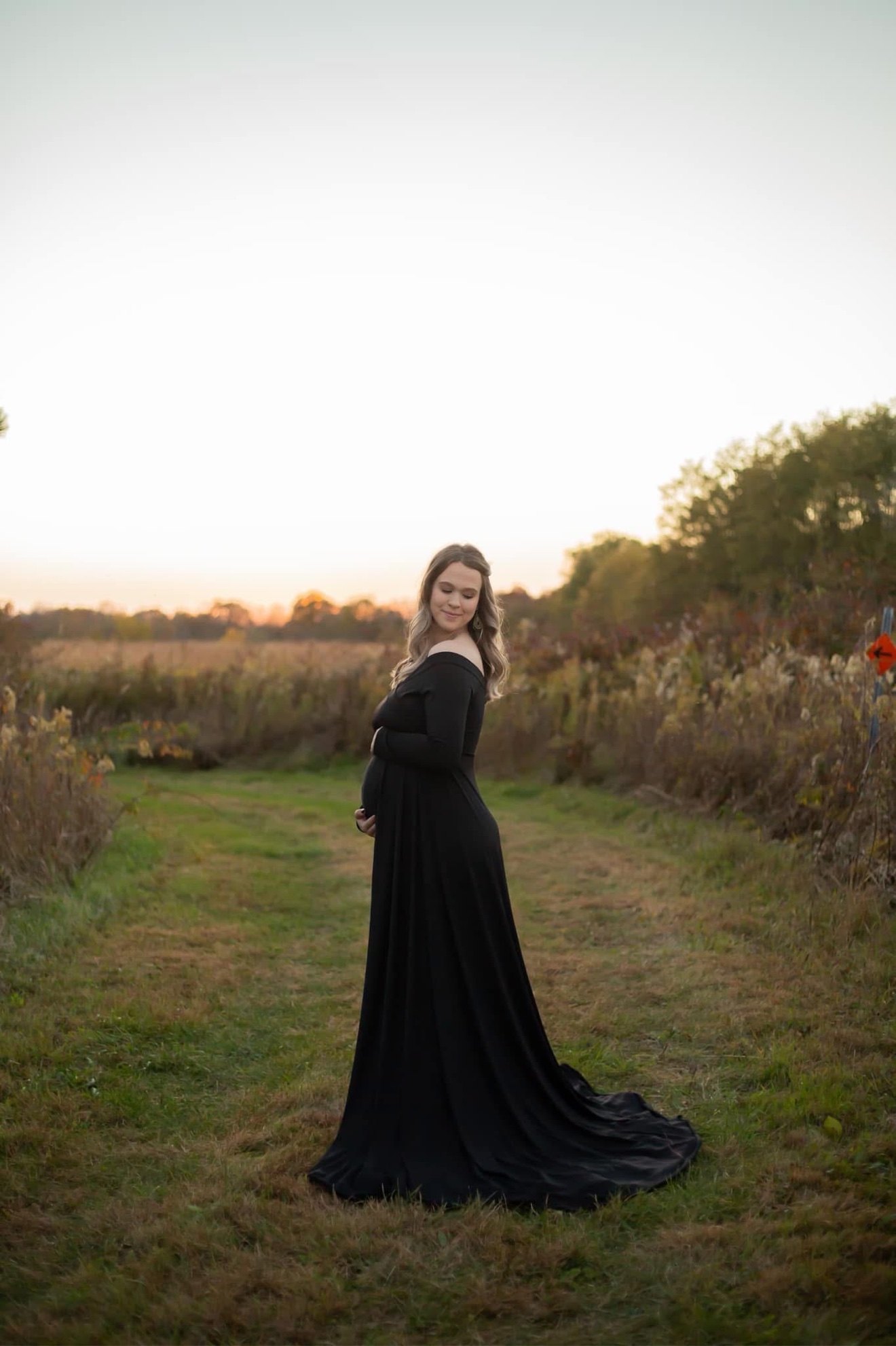 An expectant mother in a long black gown cradling her bump in a field at sunset