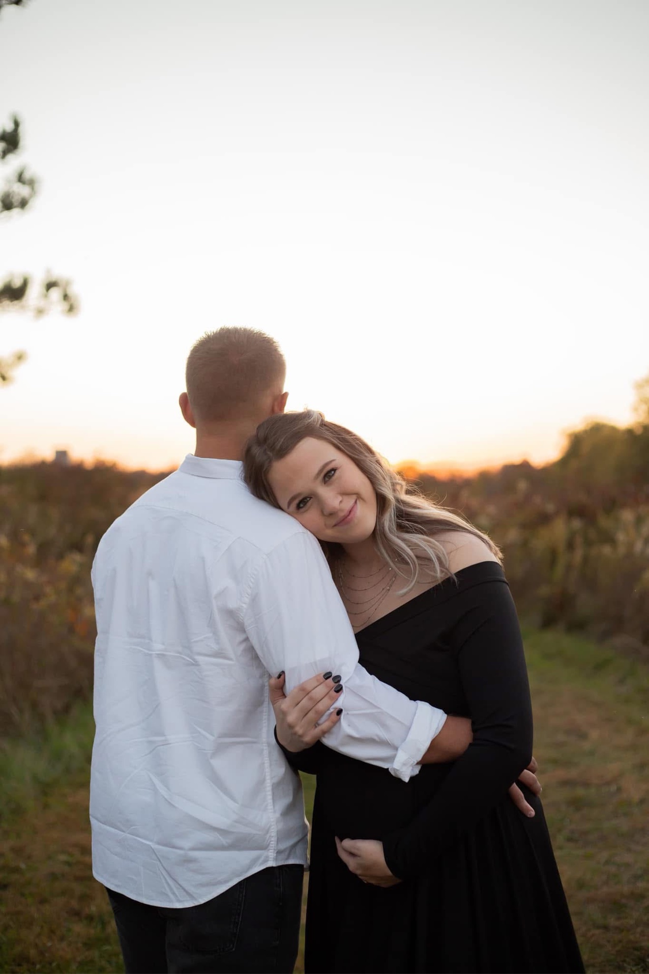 An expectant mother resting her head on her partner's shoulder at sunset