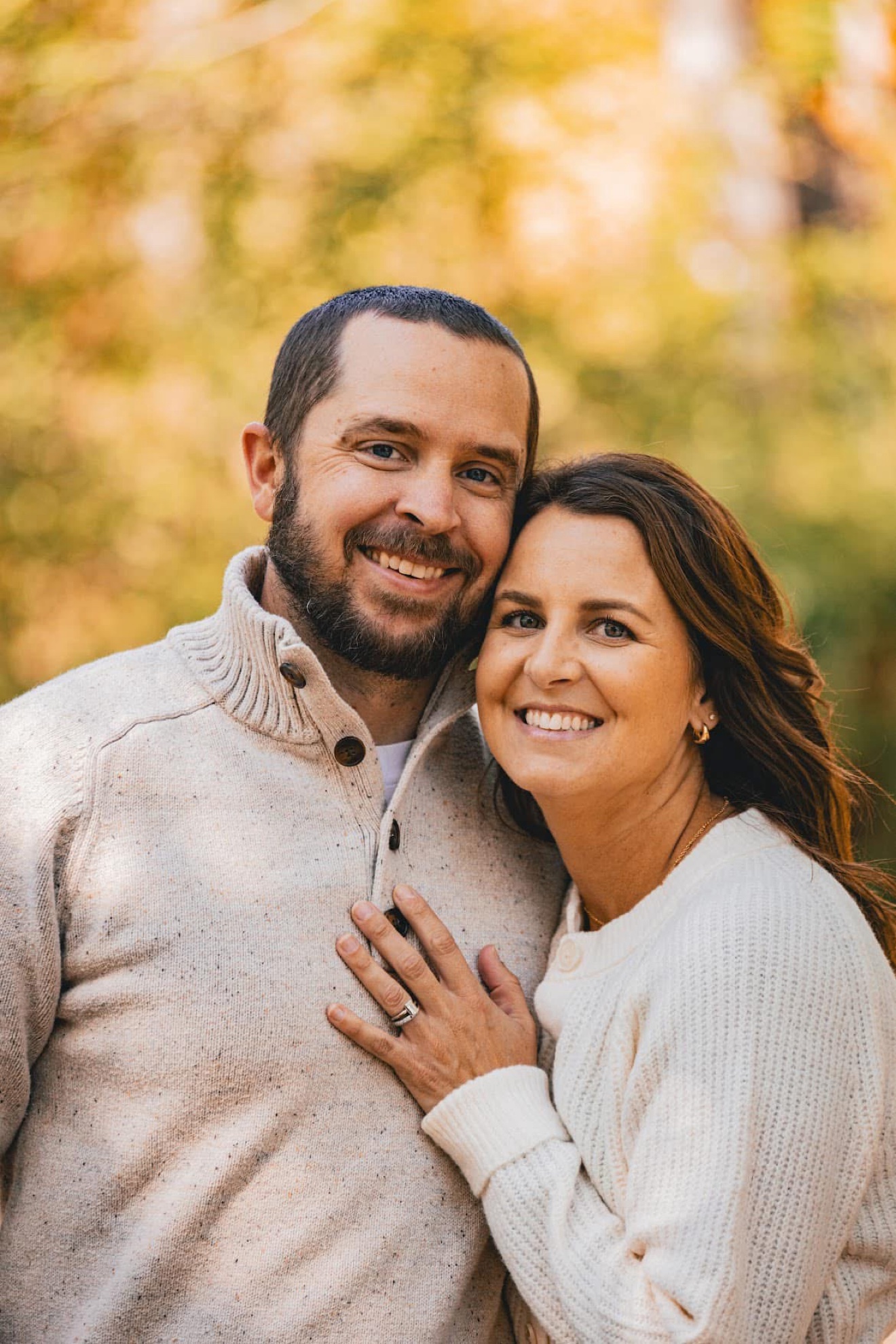 A couple in cozy sweaters smiling cheek to cheek against fall colors