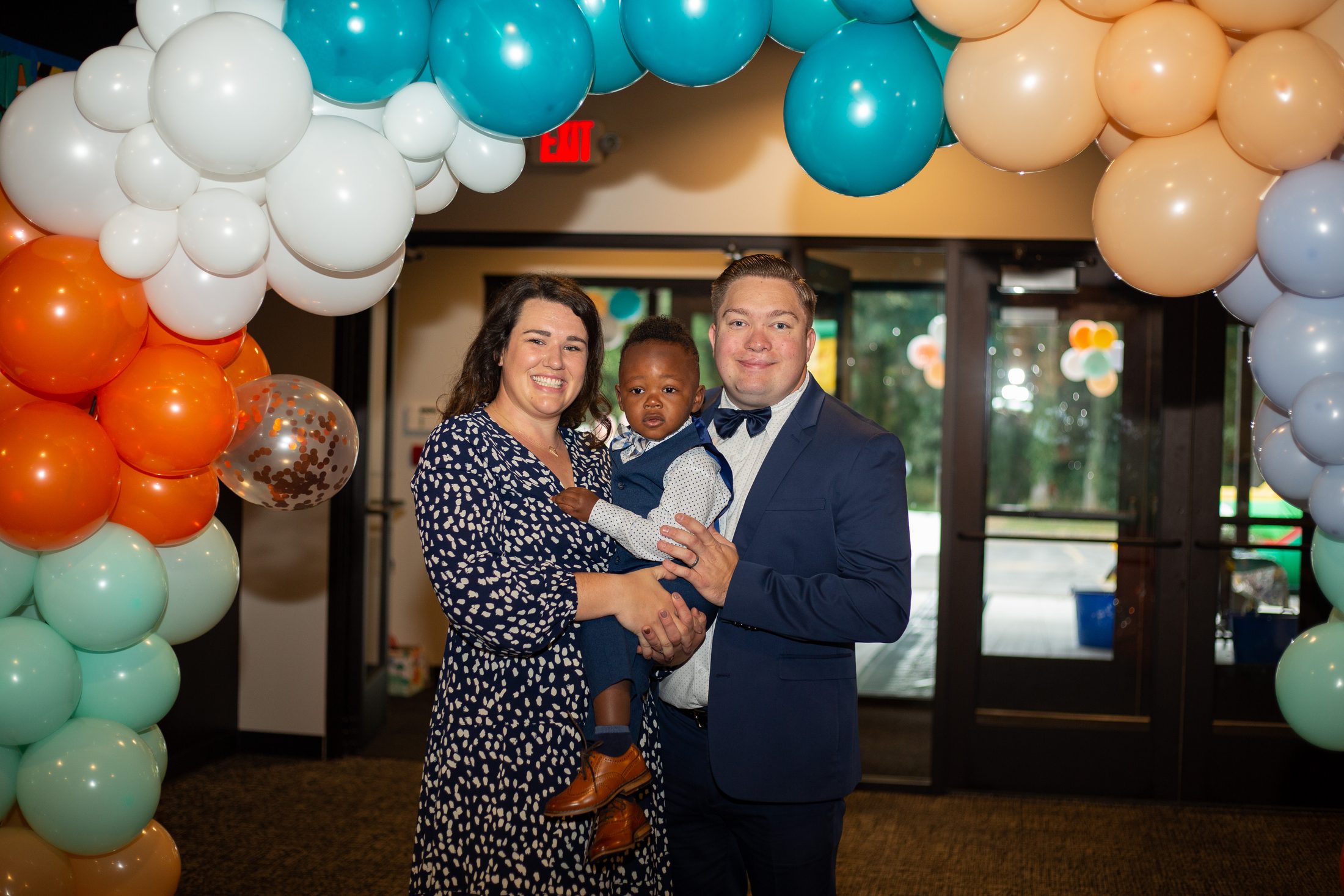 Jordan's adoption day, a family of three smiling under a balloon arch