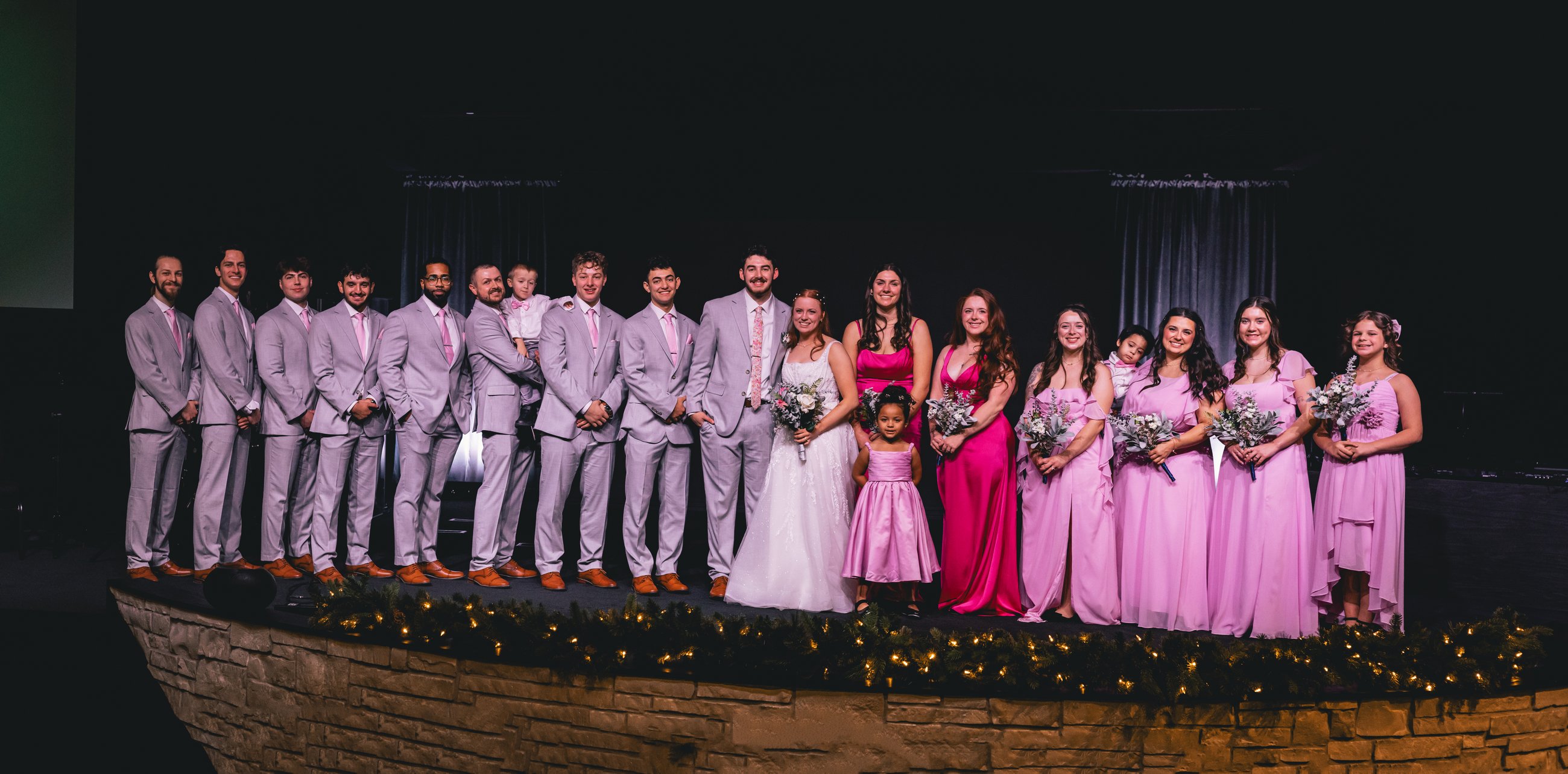 A full wedding party posed together on a stone stage